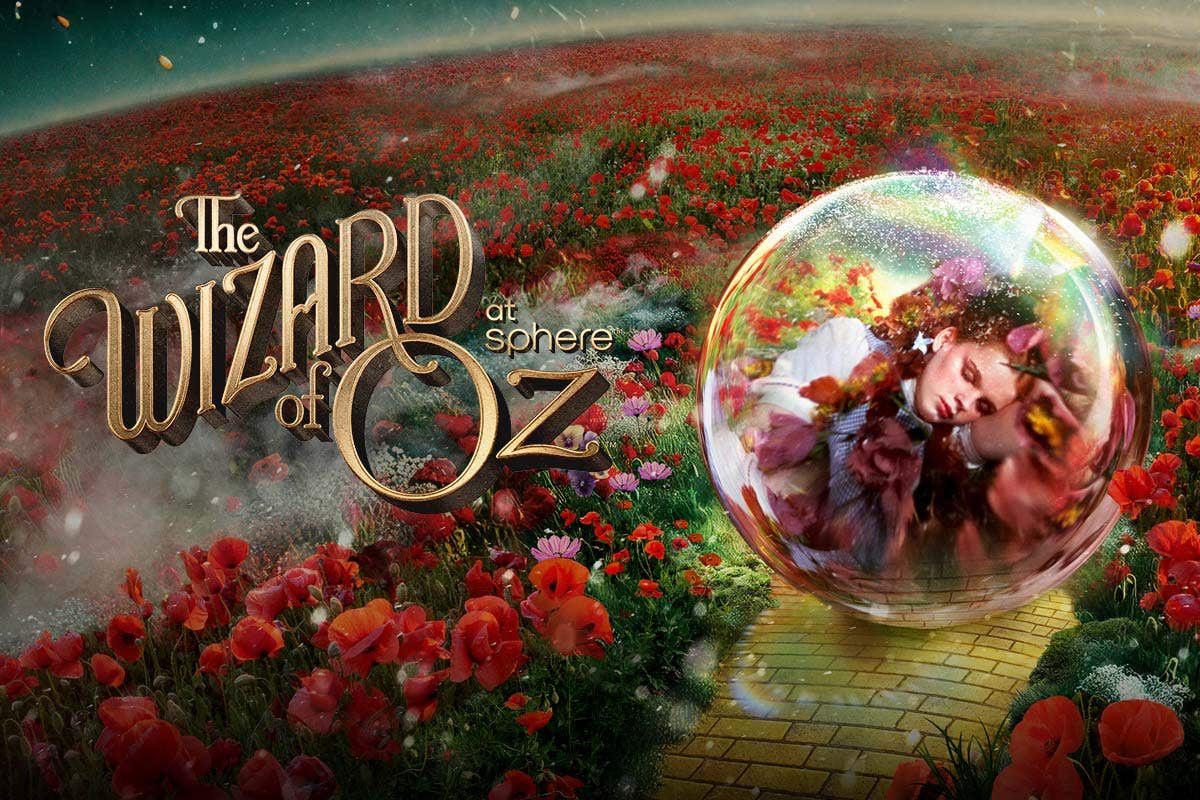 A vast field with red flowers and a yellow brick road with an transparent orb containing a visual of a girl in it, with the text The Wizard of Oz at Sphere to the left