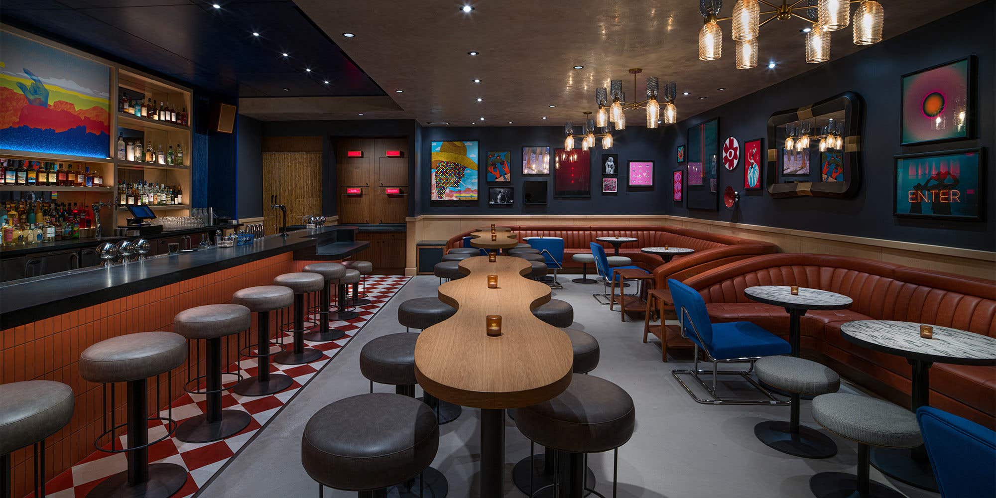 Dimly lit bar with colorful artwork on the walls with table, stool and chairs. 