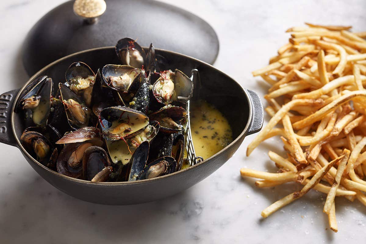 A pot of mussels in creamy sauce with a side of French fries on a marble table.