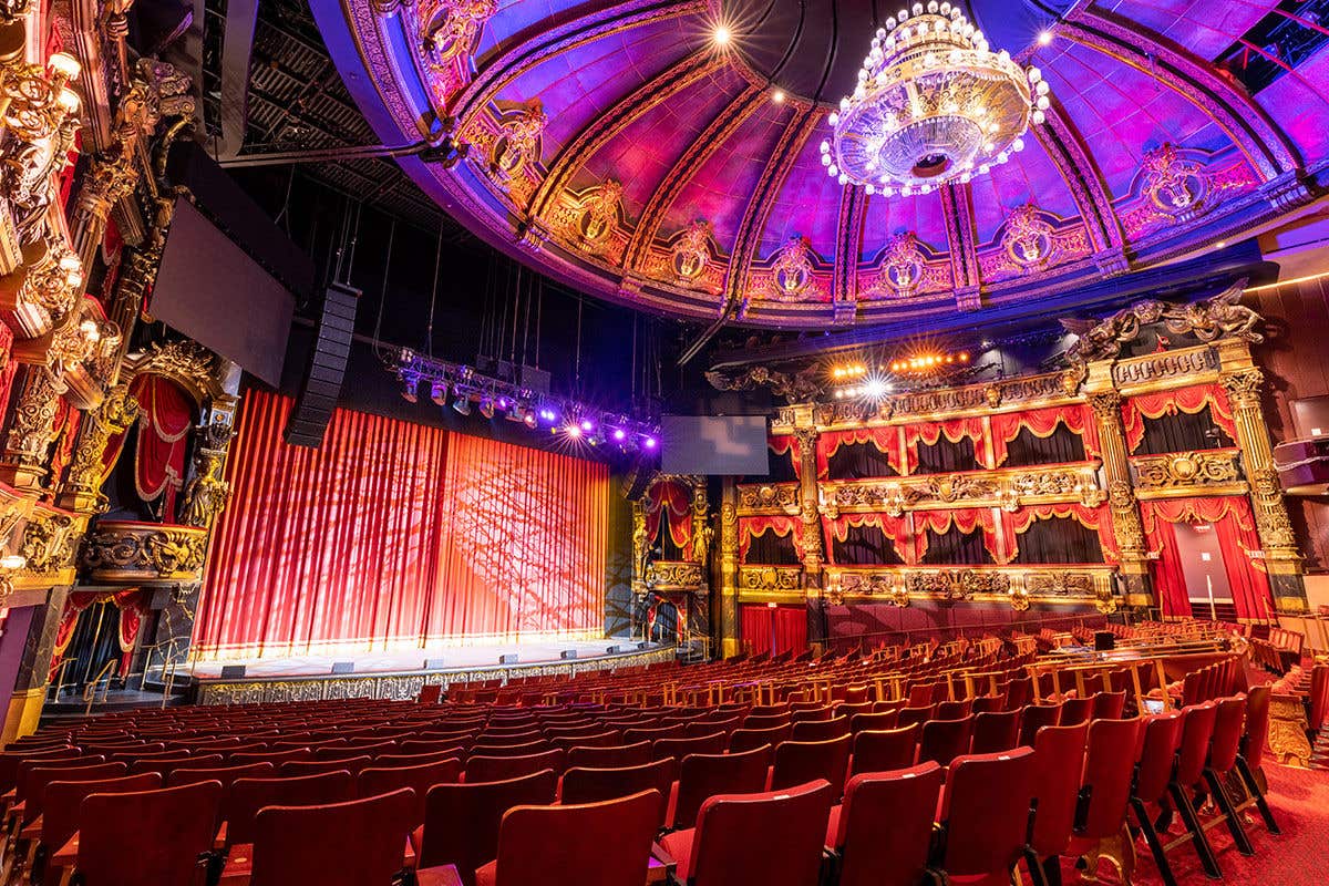 Lavishly decorated Venetian Theatre with ornate ceiling, chandelier, red velvet seats, and a brightly lit stage.