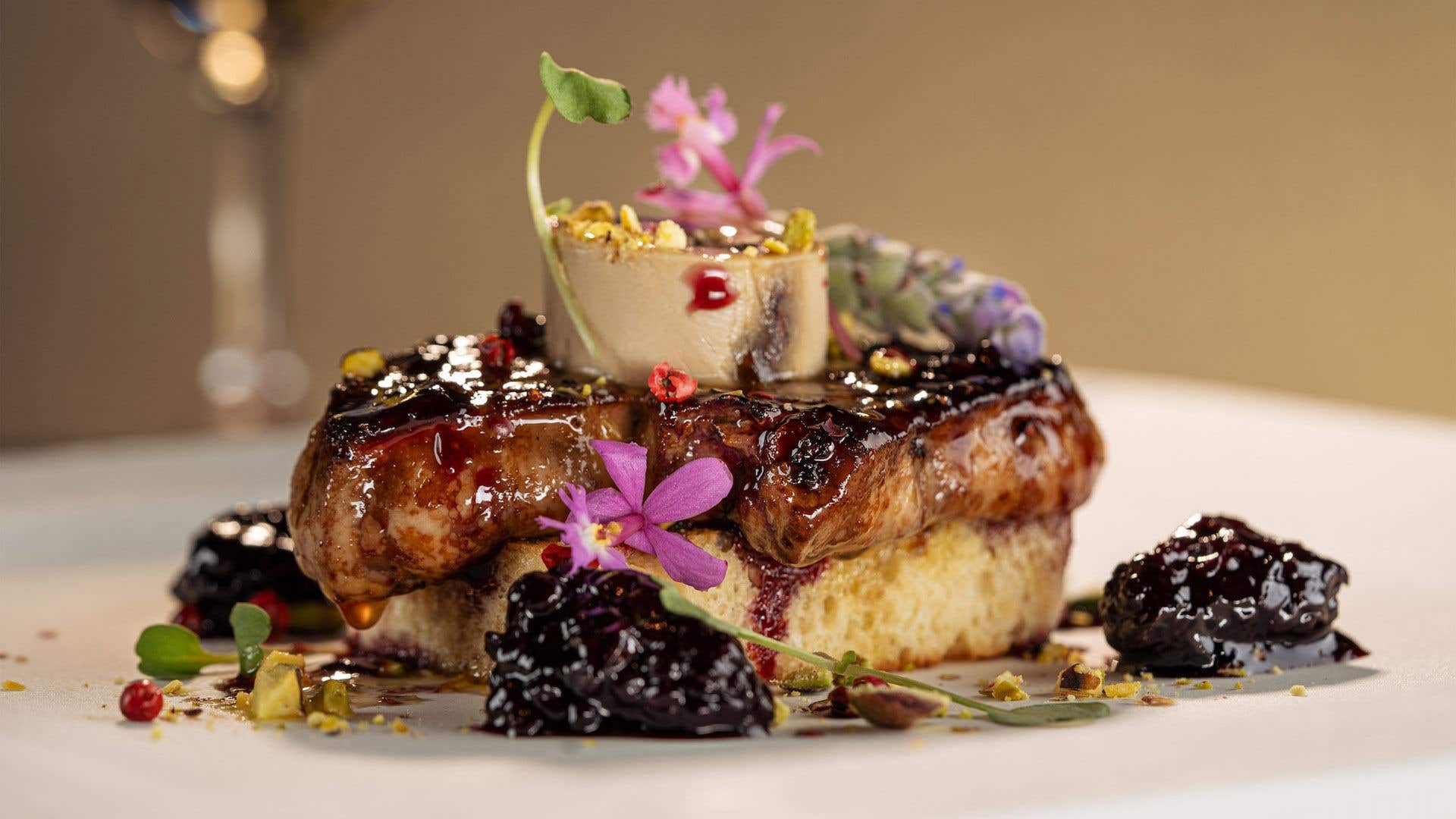 A decadent pastry dish with sauce, cooked black berries garnished with delicate flowers.
