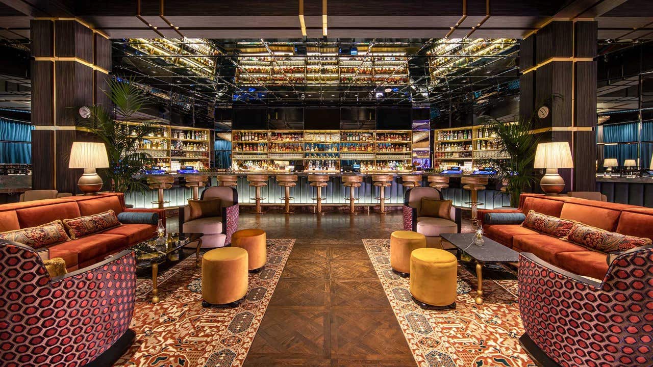 Luxurious bar lounge with plush seating, mirrored ceiling, and a well-stocked bar counter in the background.