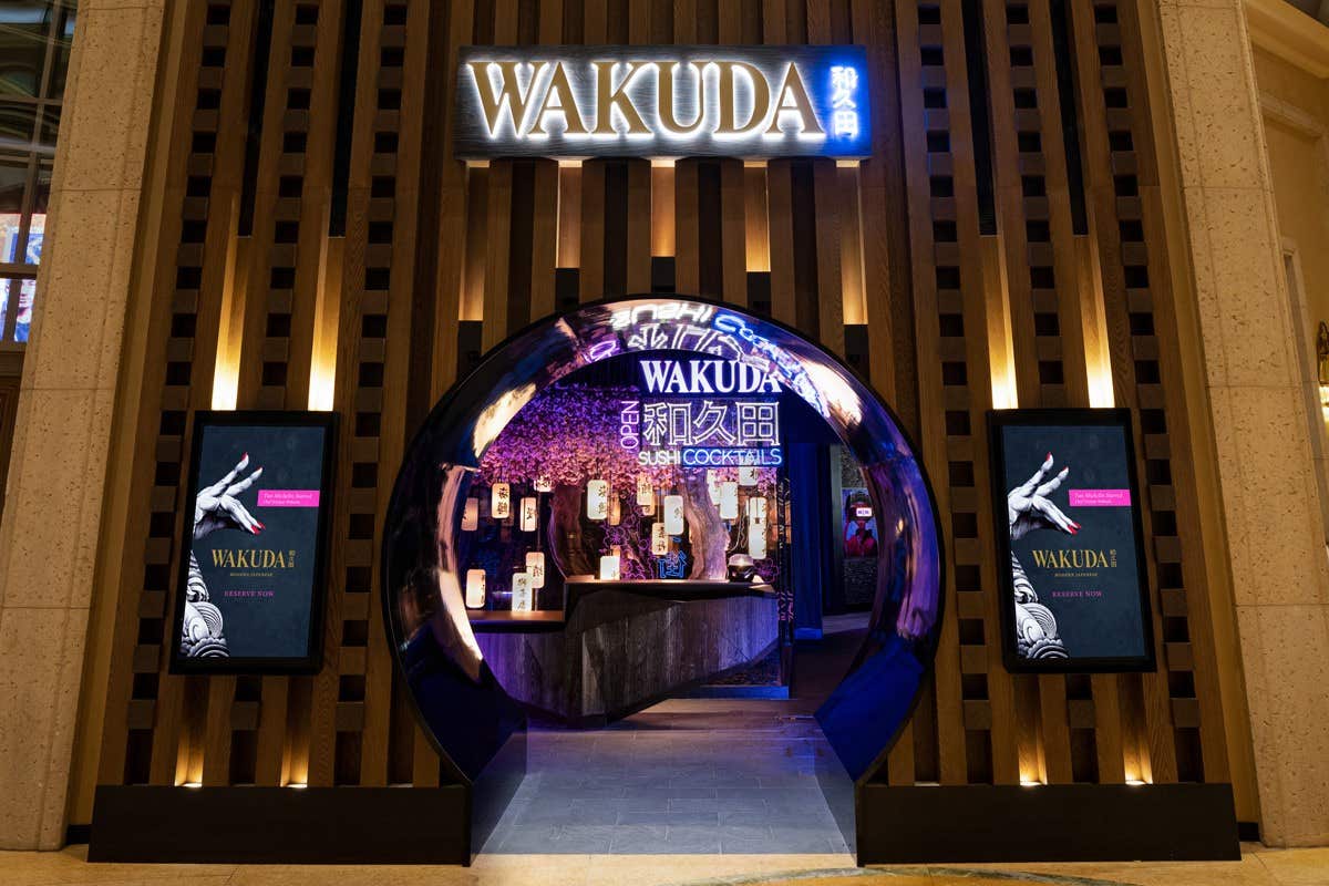 Entrance to Wakuda restaurant with illuminated signage, two digital screens, and a circular doorway featuring modern decor.