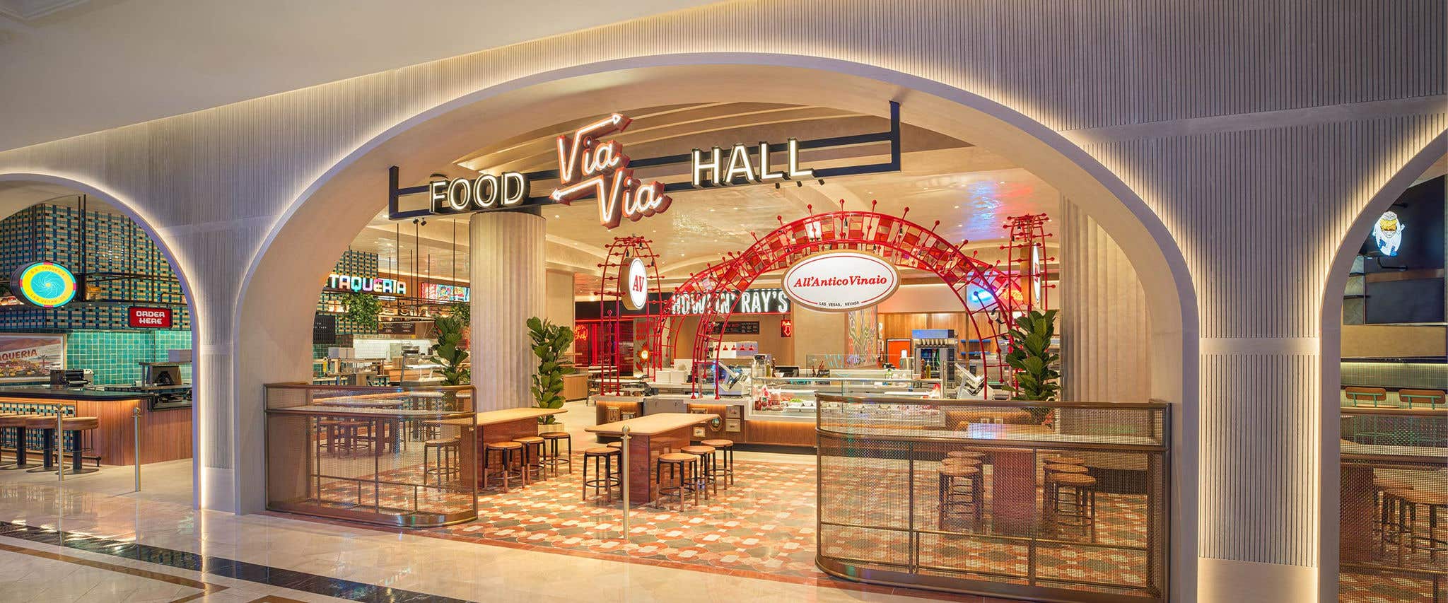 Opening to a food hall with tables, chairs and multiple restaurant fronts with a Via Via Food Hall sign in front.